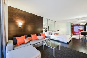 A modern hotel room with a grey sofa, a glass coffee table, a bed with white linens, and a large mirror. - SVS: Mountain View Studio | No Resort Fee | Pool & Gym | Palms Place (Las Vegas)