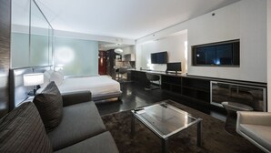 Una habitación de hotel moderna con una cama grande, un escritorio, un televisor y una zona de estar.