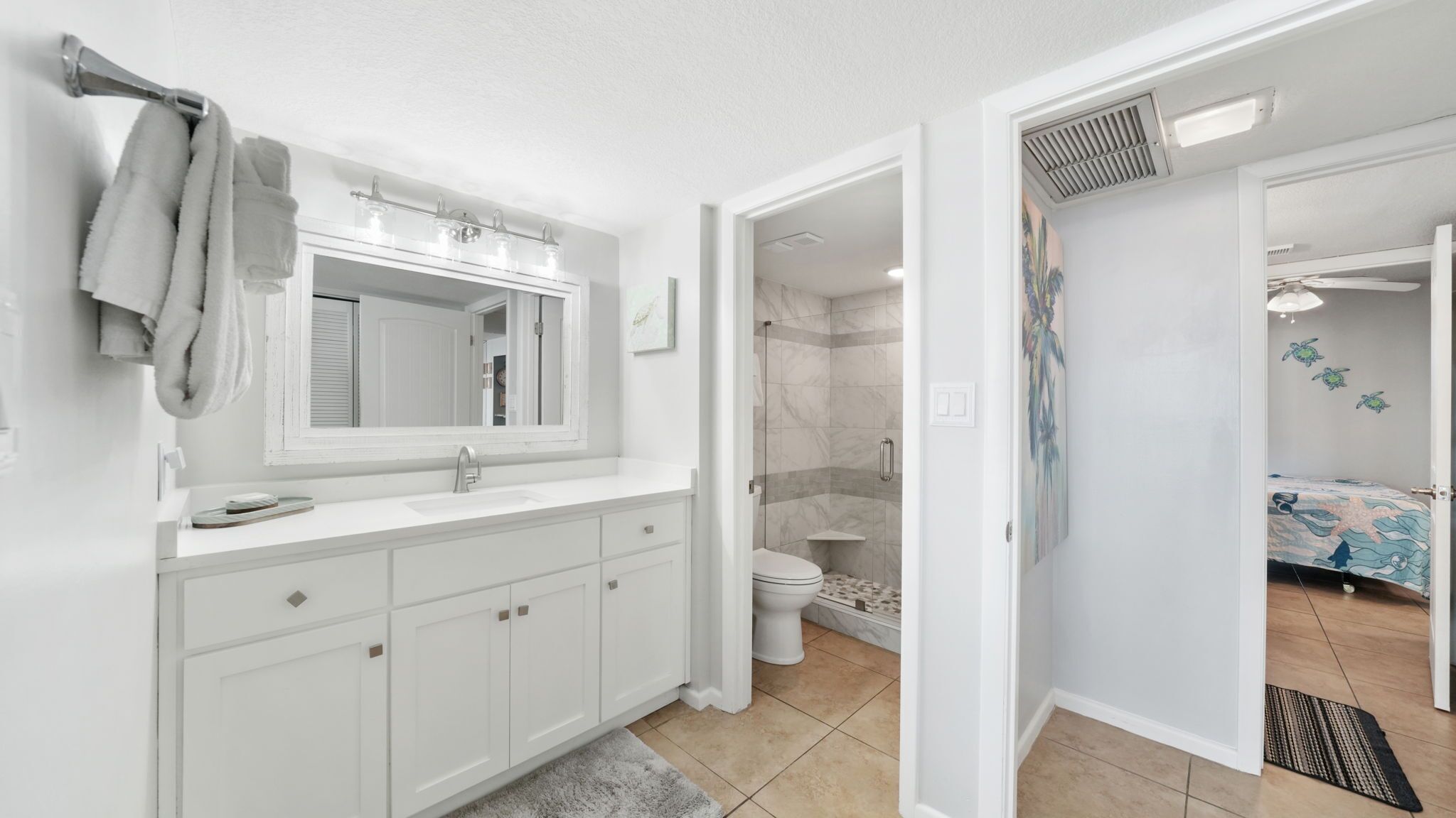 Een moderne badkamer met een wit wastafelmeubel, een douchecabine met glazen wanden en een zichtbaar toilet.