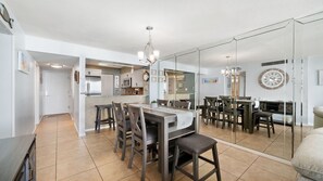 A modern kitchen with a dining area, featuring a large island, dark wooden chairs, and a chandelier. - B407- Beautifully renovated waterfront condo! Incredible Beach Rates :) (Panama City)