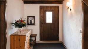 Un couloir avec une porte en bois, une petite table sur laquelle est posé un vase de fleurs et un tableau encadré accroché au mur.