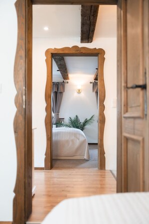 Ein Schlafzimmer mit Holztürrahmen, einem Bett mit weißer Bettdecke, einem Nachttisch und einer Wandleuchte.