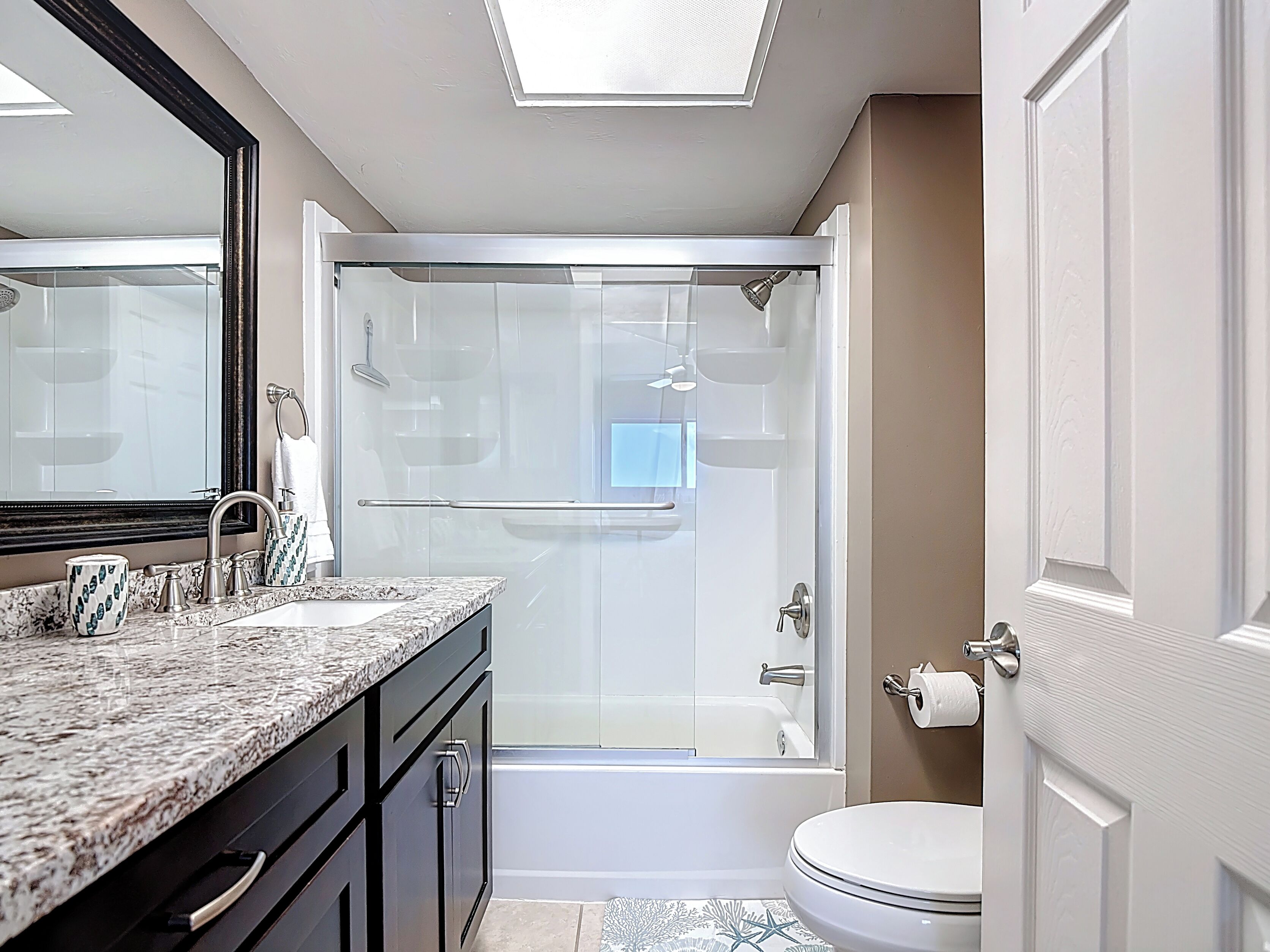 A modern bathroom with a glass-enclosed shower, a vanity with a granite countertop, and a toilet.