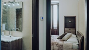 Ein modernes Schlafzimmer mit einem großen Bett, einem Nachttisch und einem kleinen Tisch. Es gibt ein Badezimmer mit Waschbecken, Spiegel und Handtuchhalter.
