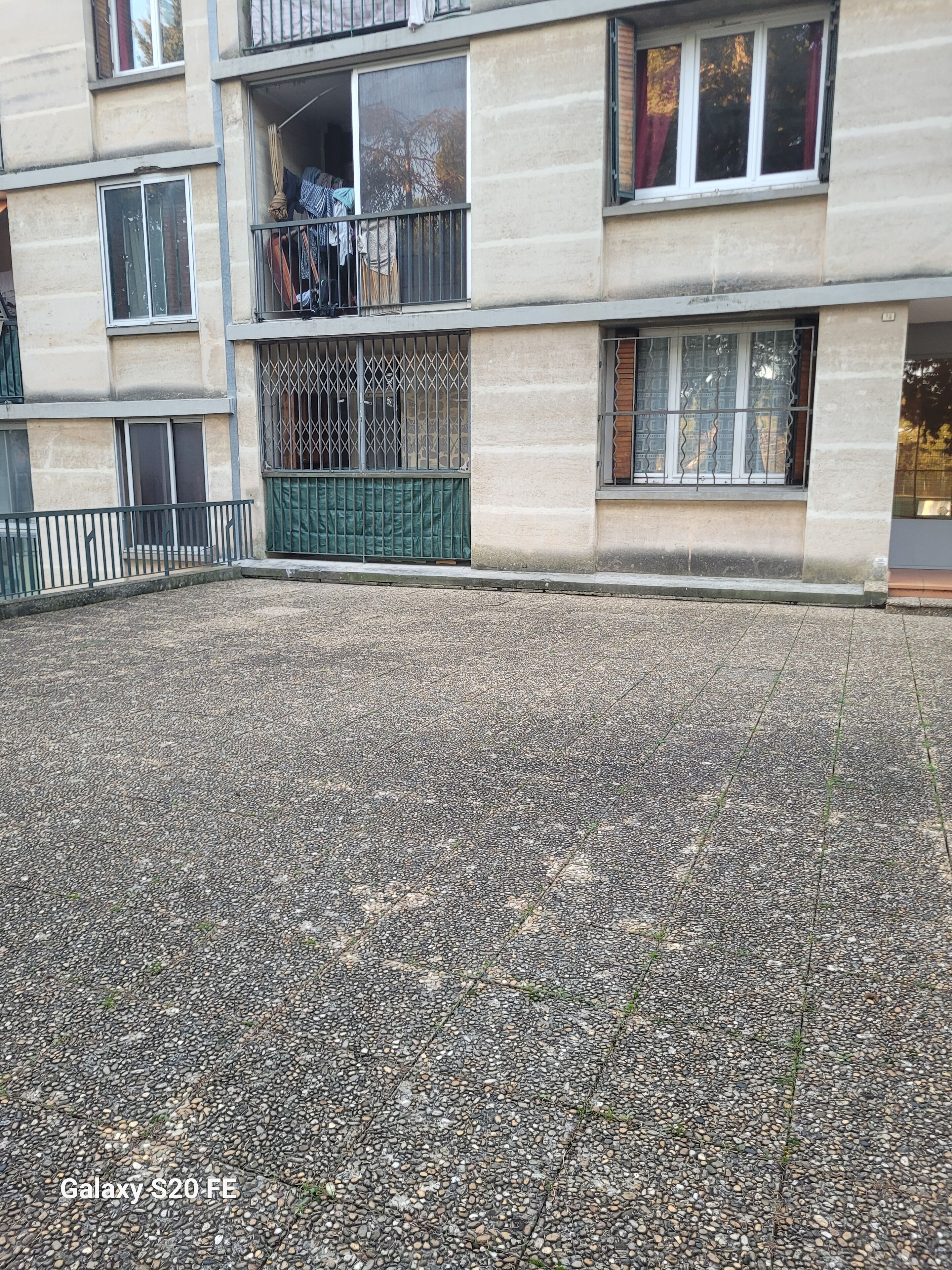 A building with multiple balconies, a gravel courtyard, and a gated entrance.