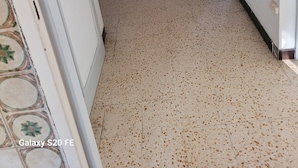 A hallway with a tiled floor, a white door, and a wall with a stone-like texture. - QUIET, SECURE F3 RENTAL WITH GARAGE (Nîmes)