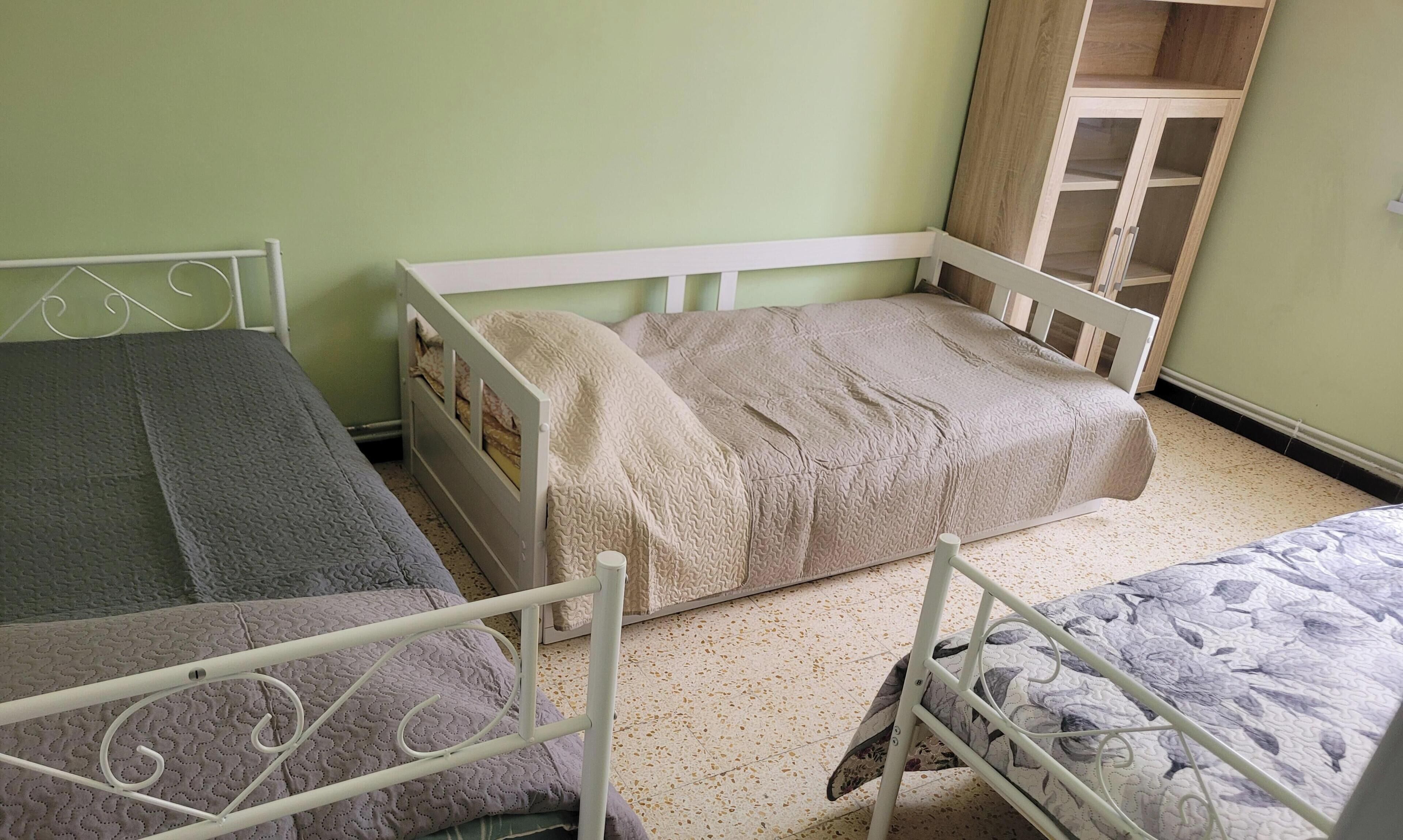 Une chambre avec deux lits simples, une armoire en bois et un mur vert.