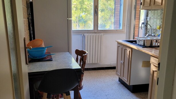 A compact kitchen with a dining table, chairs, a refrigerator, a window with a view of trees, and a sink with a faucet. - QUIET, SECURE F3 RENTAL WITH GARAGE (Nîmes)