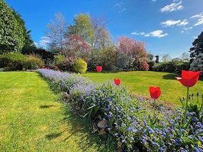 Un jardín con césped cuidado, diversas plantas florecientes y árboles con follaje otoñal.