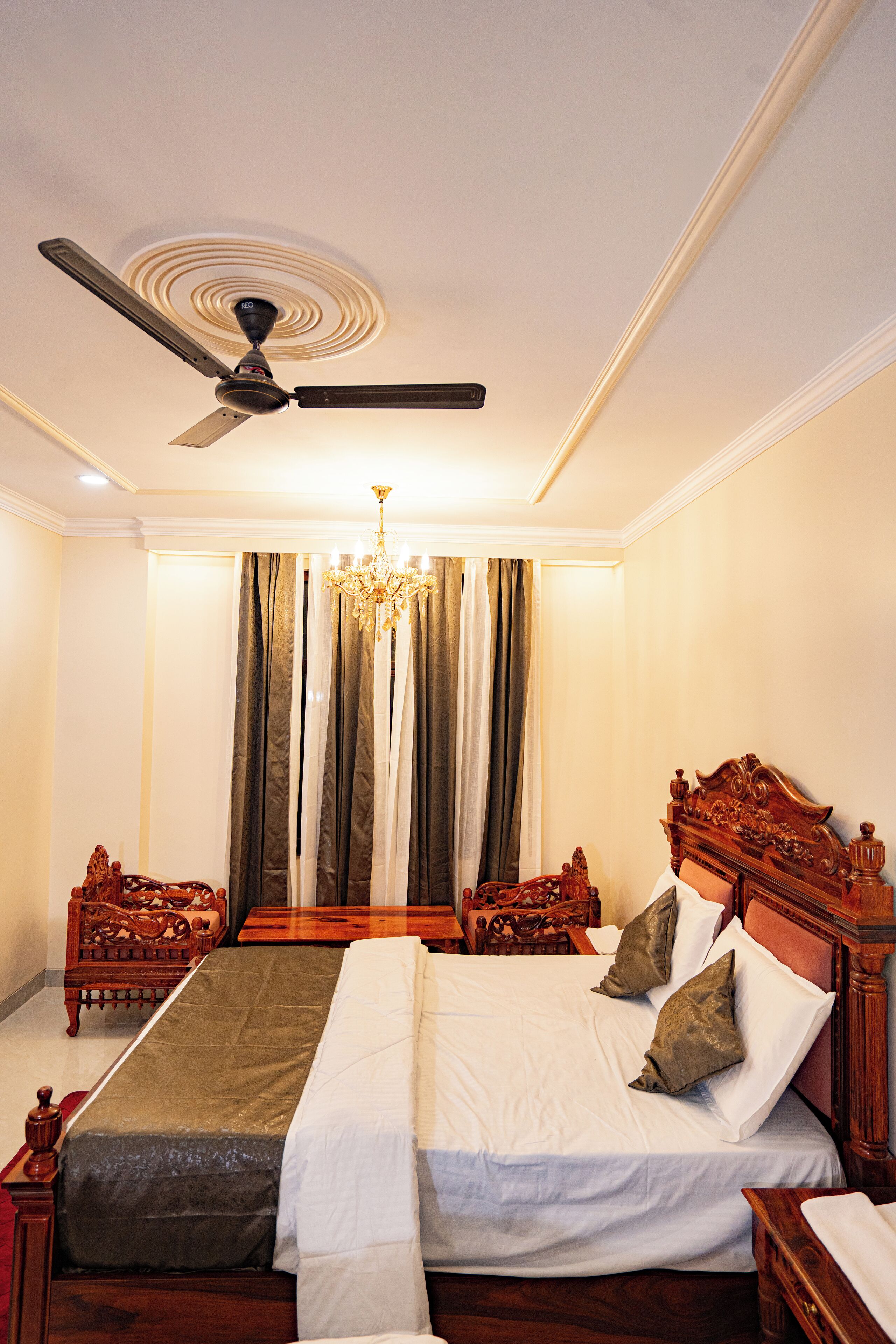 A bedroom with a large bed, a ceiling fan, a chandelier, and curtains.