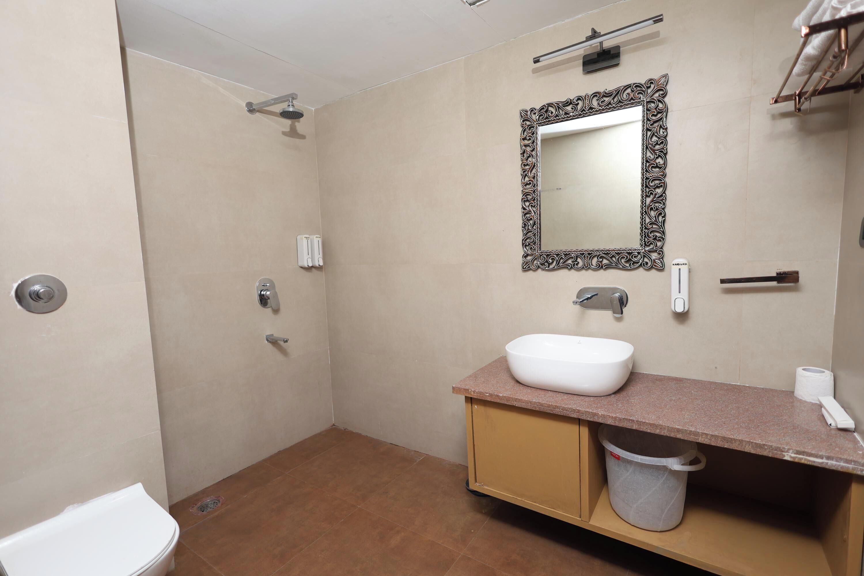A bathroom with a shower, toilet, sink, and a mirror with an ornate frame.