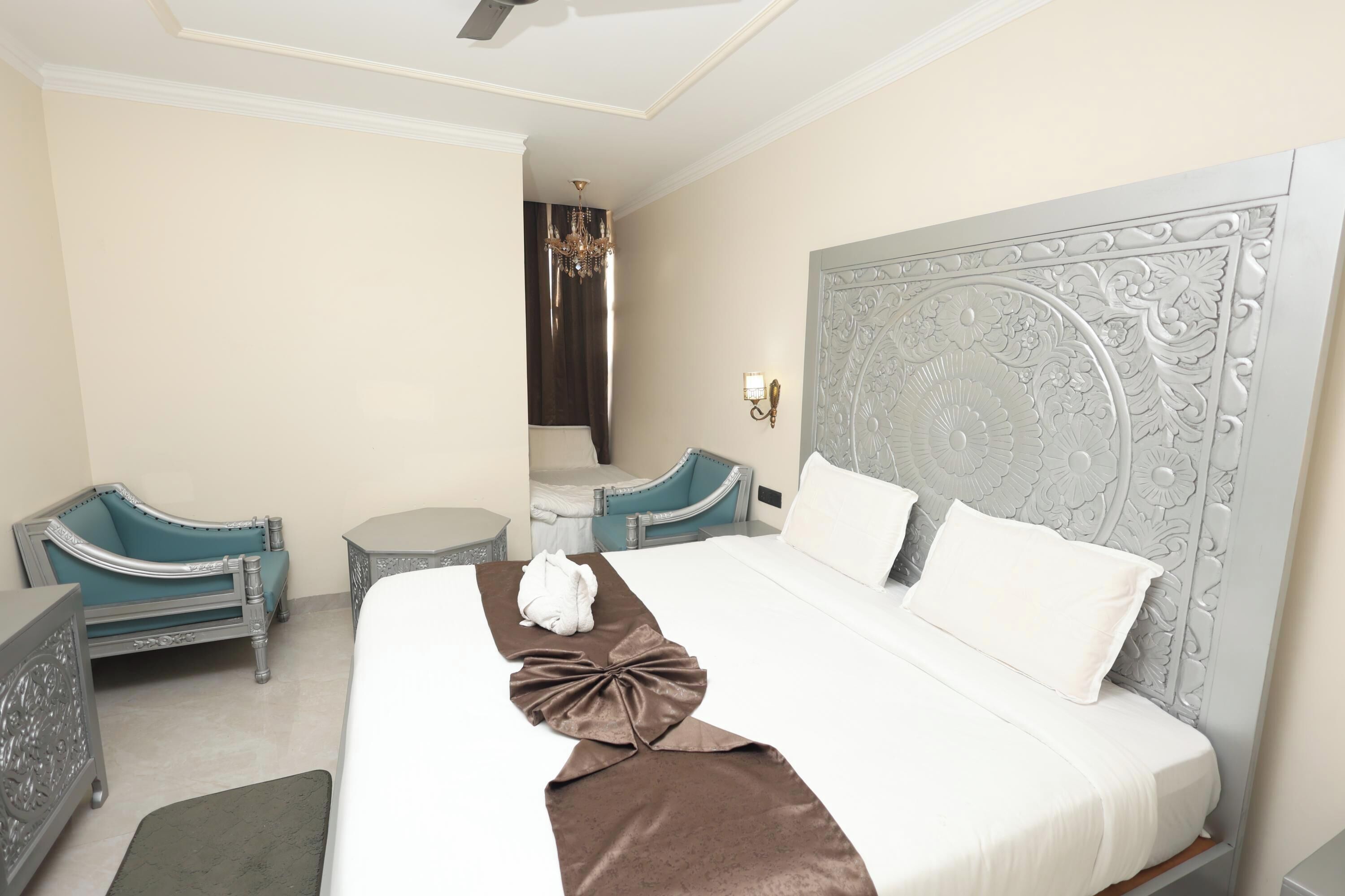 Una habitación de hotel con una cama grande, dos sillones, una mesita y una araña.