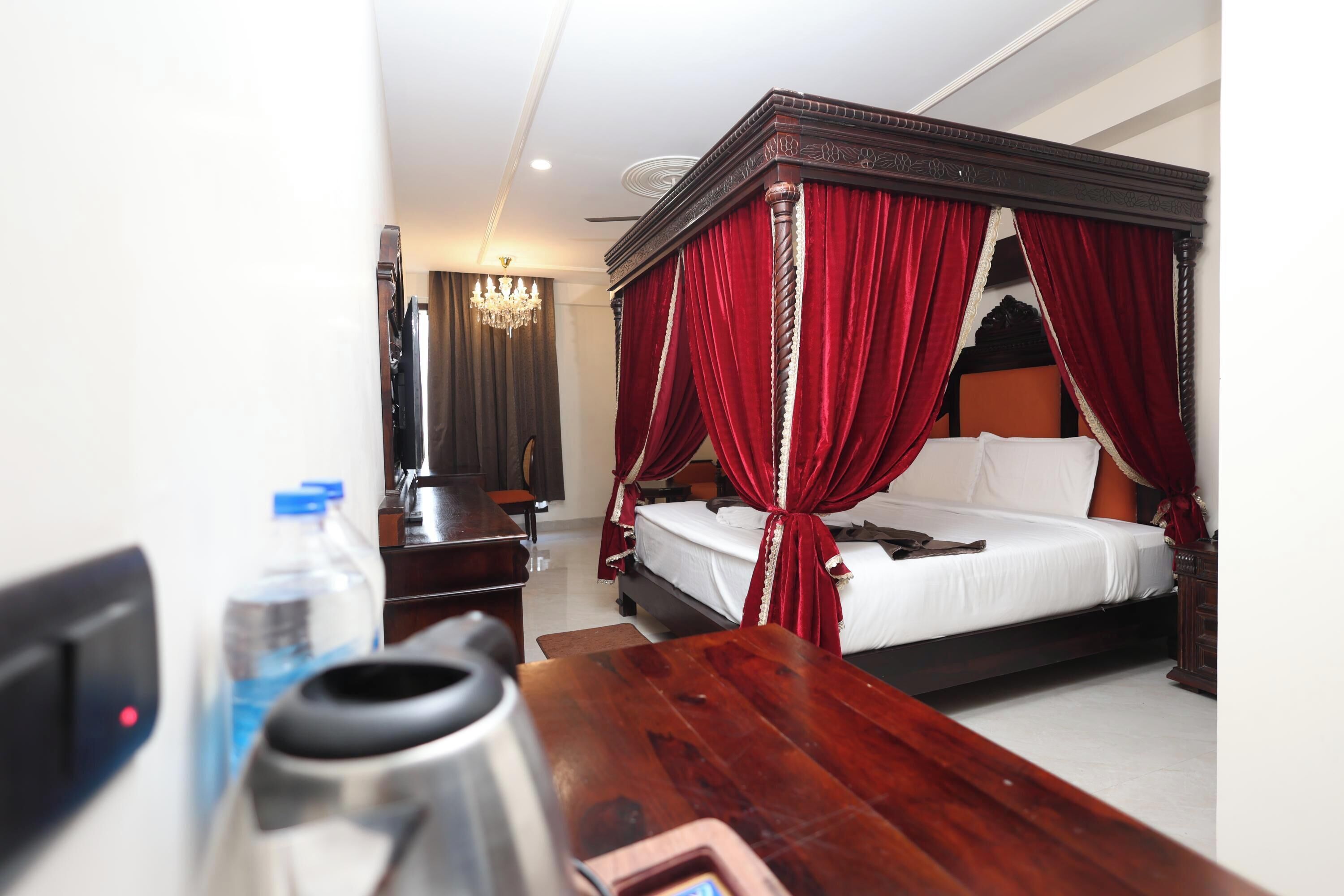 A four-poster bed with red drapes, a wooden table, a water bottle, and a kettle.
