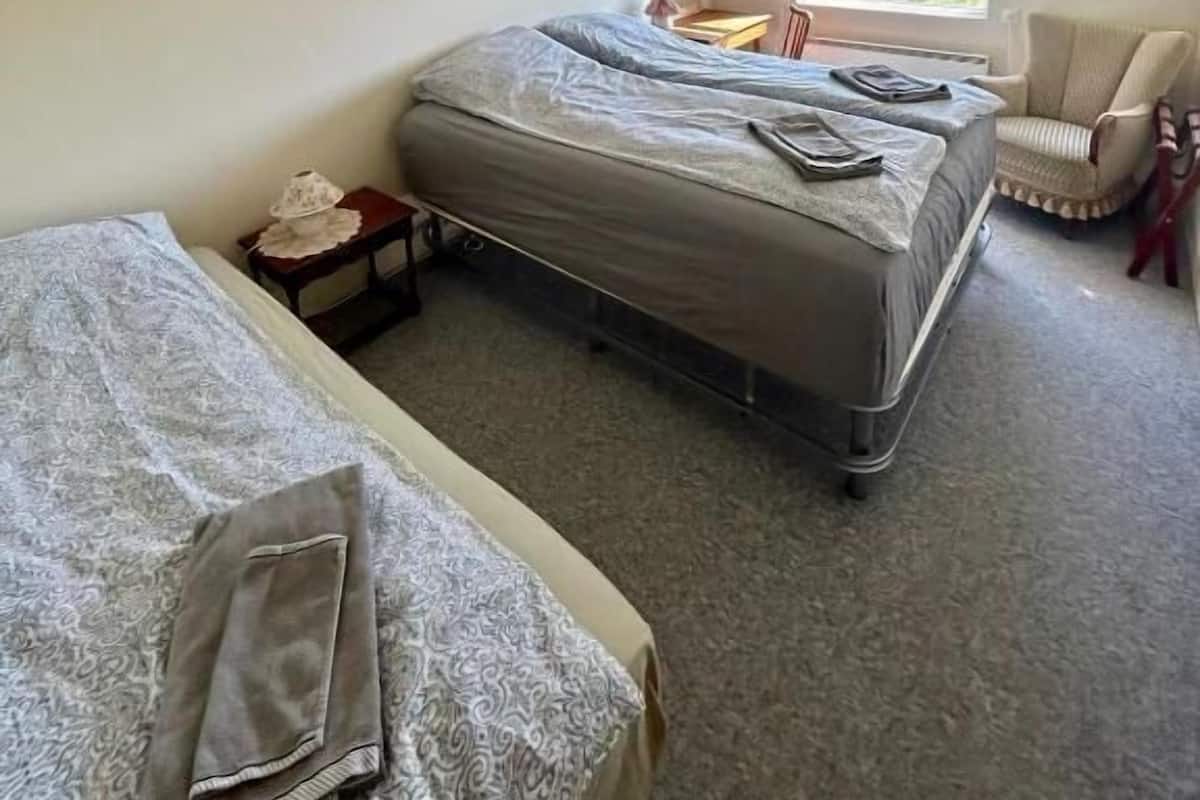 Habitación individual pequeña con cama, una silla, una mesita y ventana con vistas al exterior.