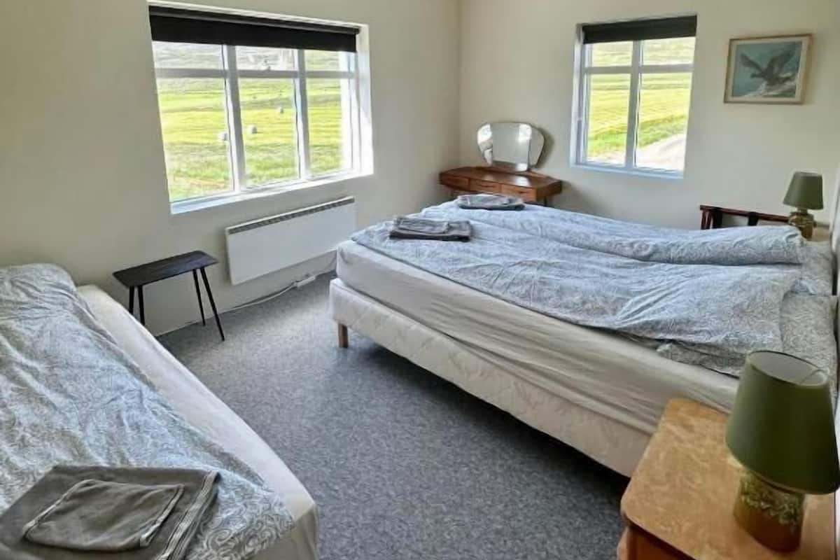 Una habitación con dos camas, una mesita, una lámpara y una ventana con vistas a zonas verdes.