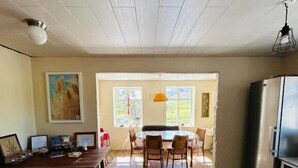 A spacious kitchen with wooden flooring, a dining area with chairs, a refrigerator, and a ceiling light fixture.