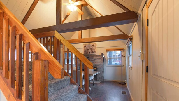 A staircase with wooden railings leading to a room with a stone fireplace, a dining table, and a window. - The Heavenly Foothills For 4 (South Lake Tahoe)