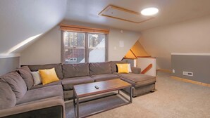 A cozy loft bedroom with a sectional sofa, a small table, and a window with a view of the outside. - The Heavenly Foothills For 4 (South Lake Tahoe)