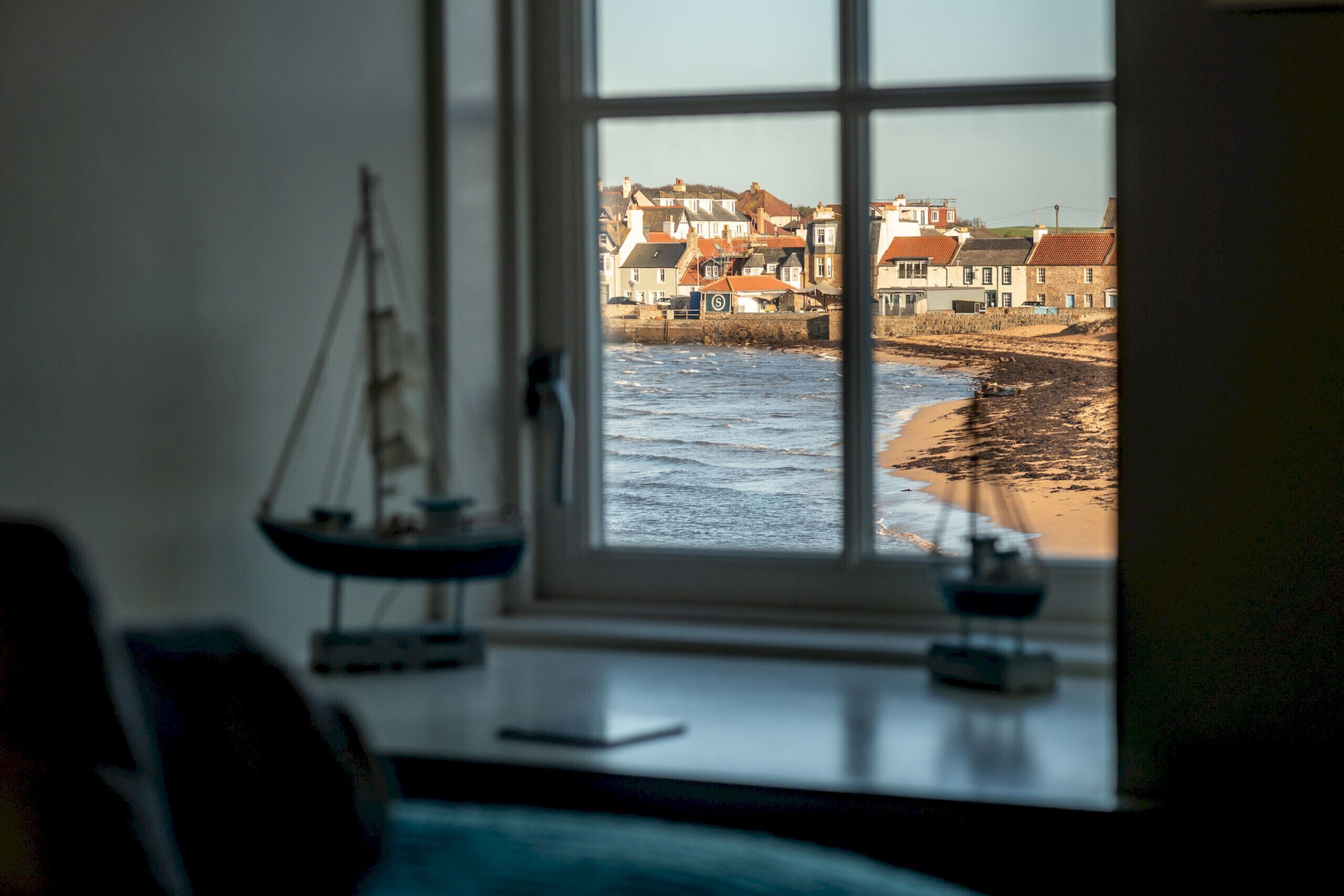 Ein Zimmer mit Blick auf einen Strand und Häuser durch ein Fenster.