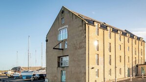 Un edificio grande de varios pisos con techo plano, probablemente un hotel o albergue, ubicado cerca de un muelle con barcos amarrados.