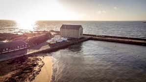 Un edificio costero con un muelle que se adentra en el agua, una playa de arena y una vista despejada del mar.