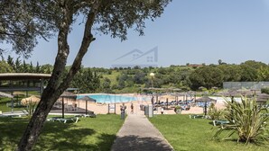 Zona de piscina con sillones de descanso y sombrillas, rodeada de vegetación y un cielo despejado.