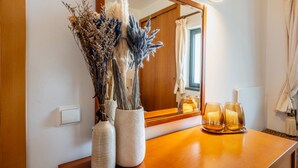 Un baño con tocador de madera, dos jarrones de cerámica con plantas secas y dos velas sobre la encimera.