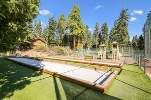 A pool table with a surrounding green artificial turf area, a wooden bench, and a playground with climbing structures and a slide. - Rocky Ridge Unit #35 (Tahoe City)