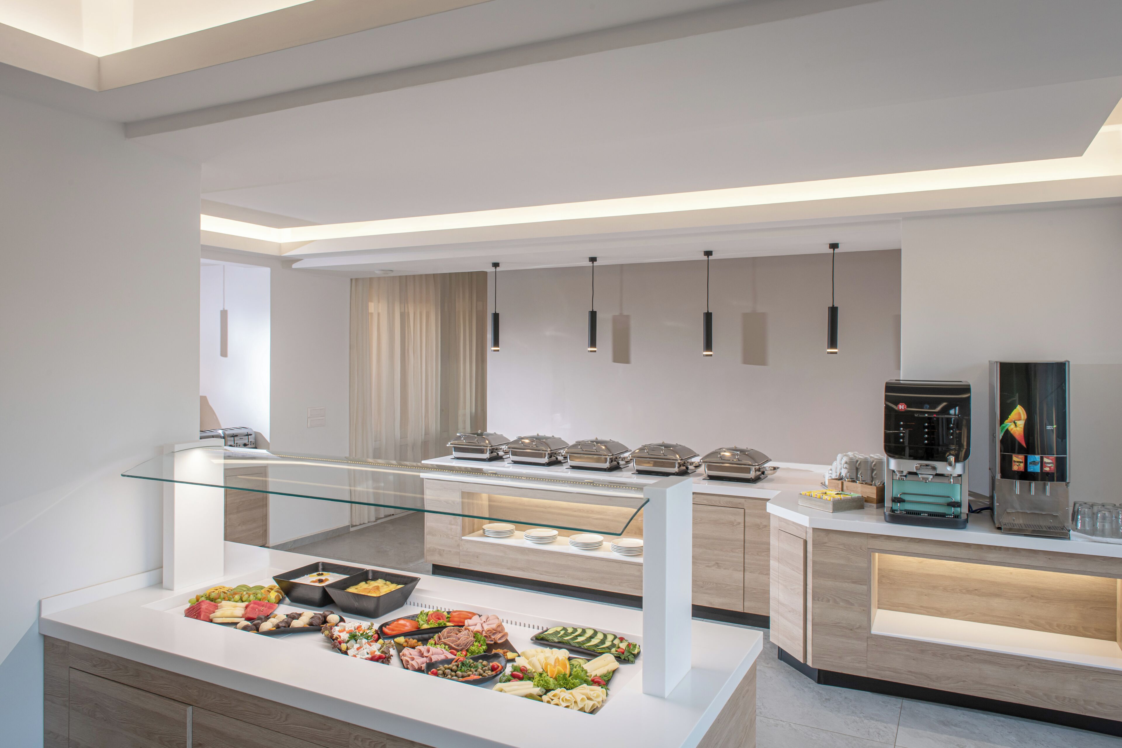 A modern hotel buffet with glass display cases, a coffee machine, and a water dispenser.