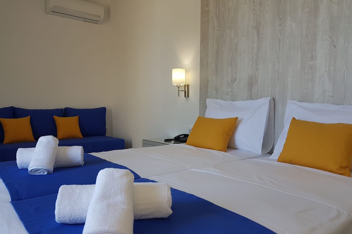 A hotel room with two beds, a blue sofa, and a nightstand with a phone.