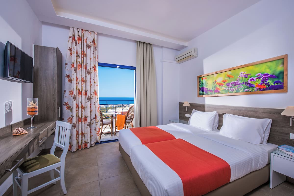 A hotel room with a bed, a desk with a chair, a TV, a painting, and a window with curtains.