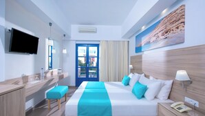 A hotel room with a bed, bedside table, a desk with a chair, a TV, and a window with curtains. - Astra Village (Koutouloufari)