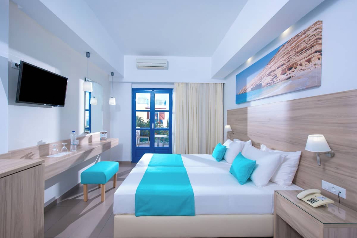 A hotel room with a bed, bedside table, a desk with a chair, a TV, and a window with curtains.