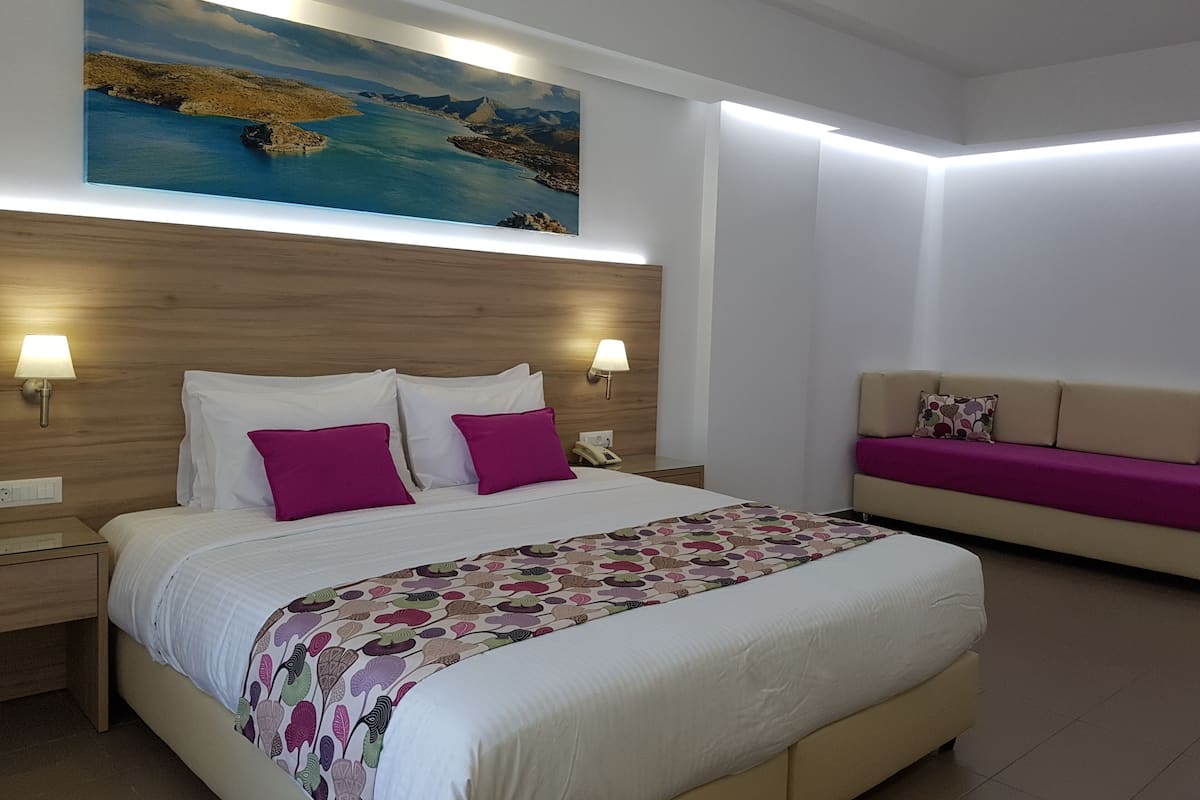 A hotel room with a bed, bedside lamps, a painting, a sofa, and a patterned bedspread.