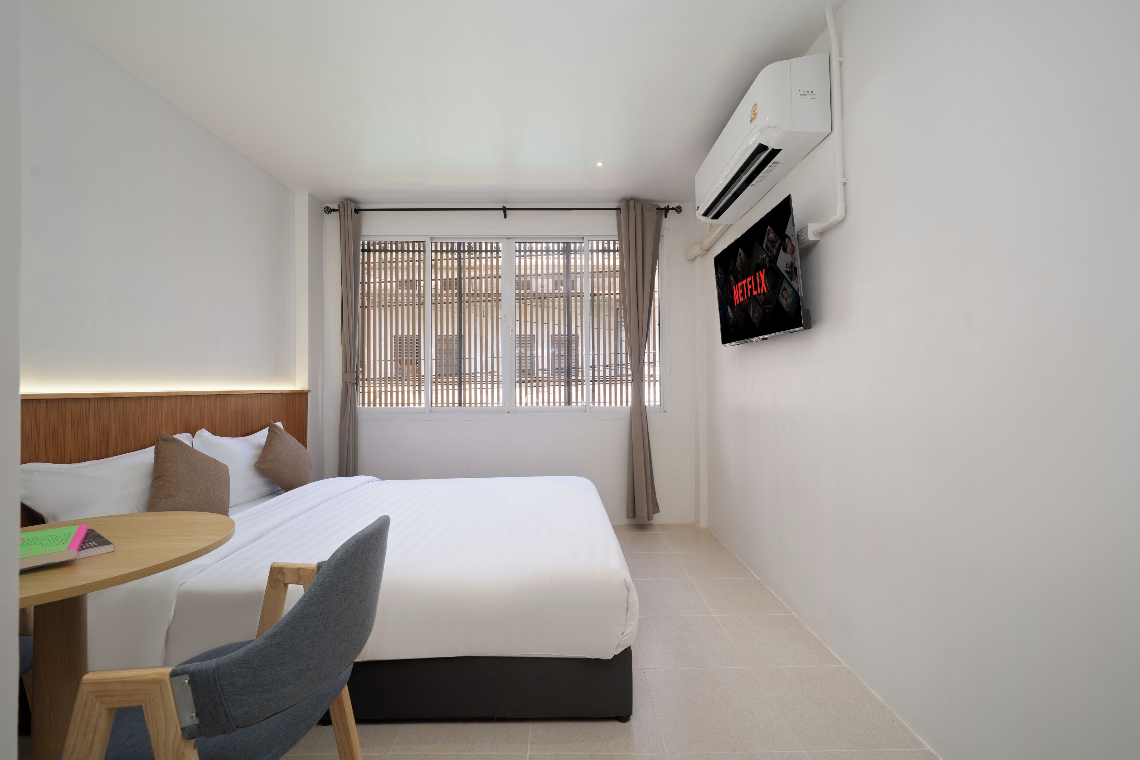 Ein Hotelzimmer mit Bett, Schreibtisch, Stuhl, Fernseher und Klimaanlage.
