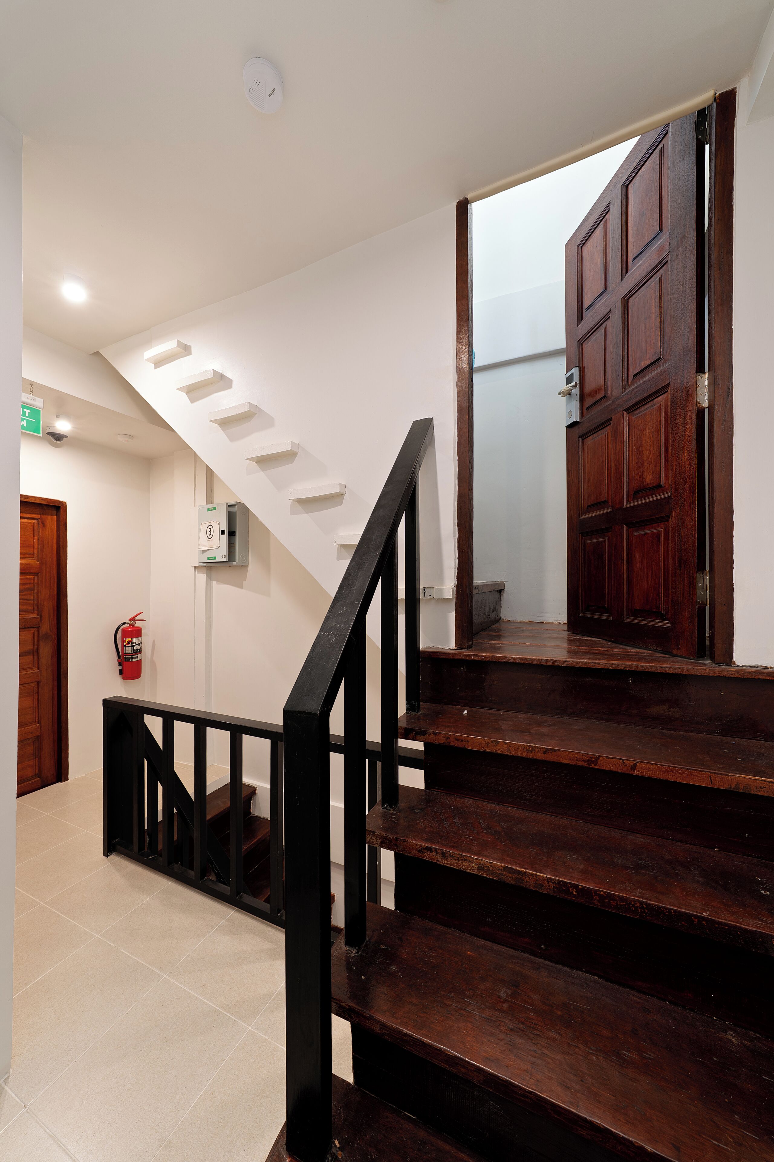 A staircase with wooden steps and black railings, leading to a room with a wooden door and a fire extinguisher on the wall.