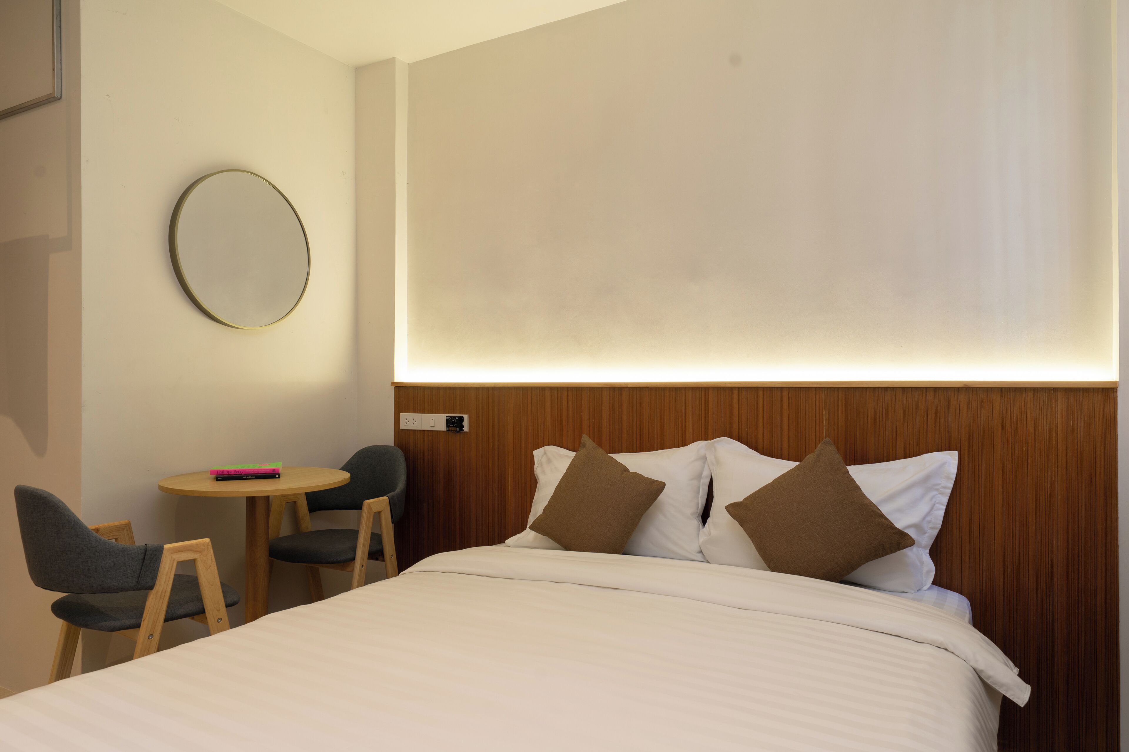 Une chambre d’hôtel avec un lit, un miroir rond, une petite table ronde et deux chaises.