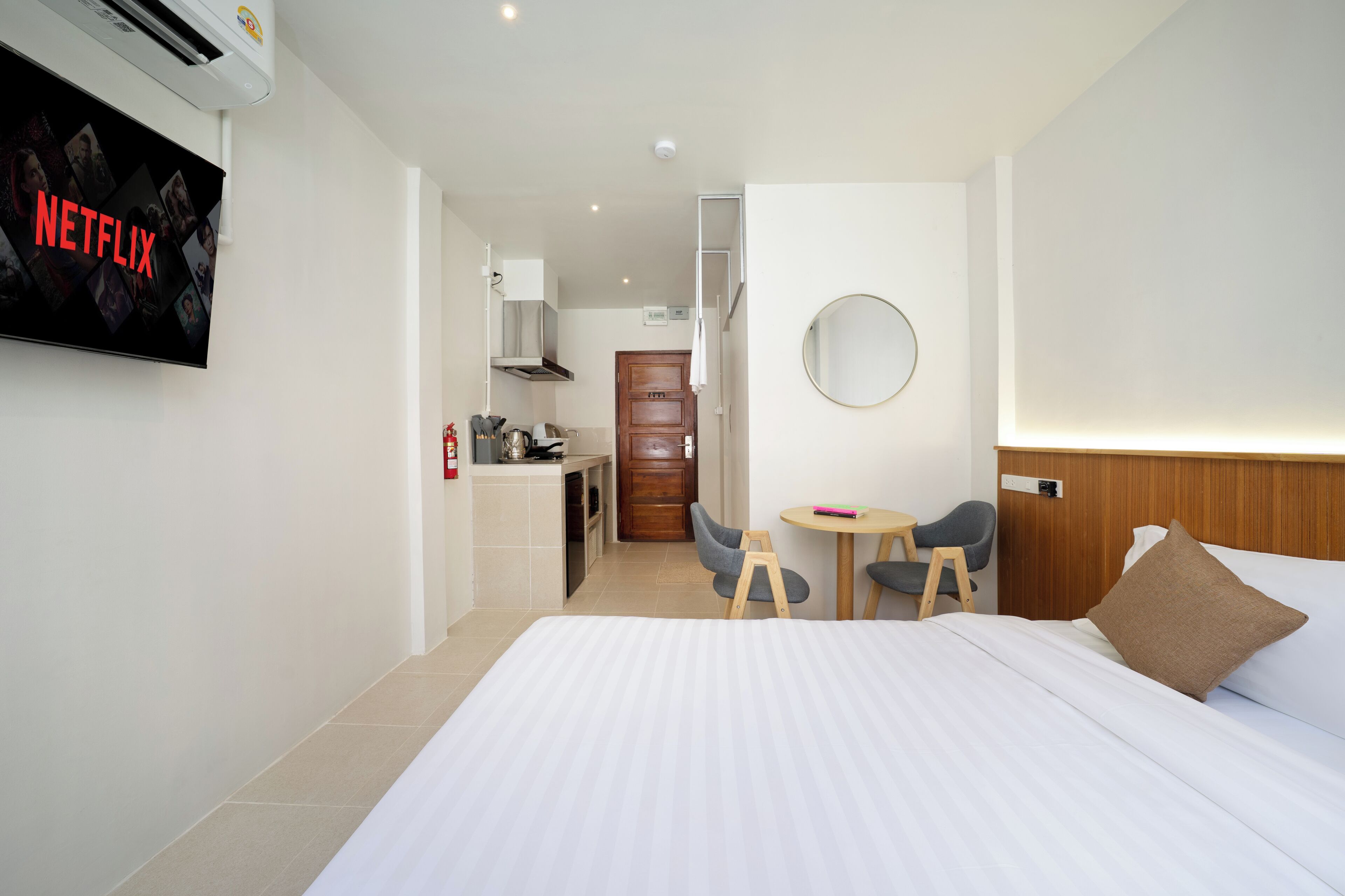 Une chambre d’hôtel comprenant un lit, un bureau avec une chaise, une petite table, un miroir et une kitchenette.
