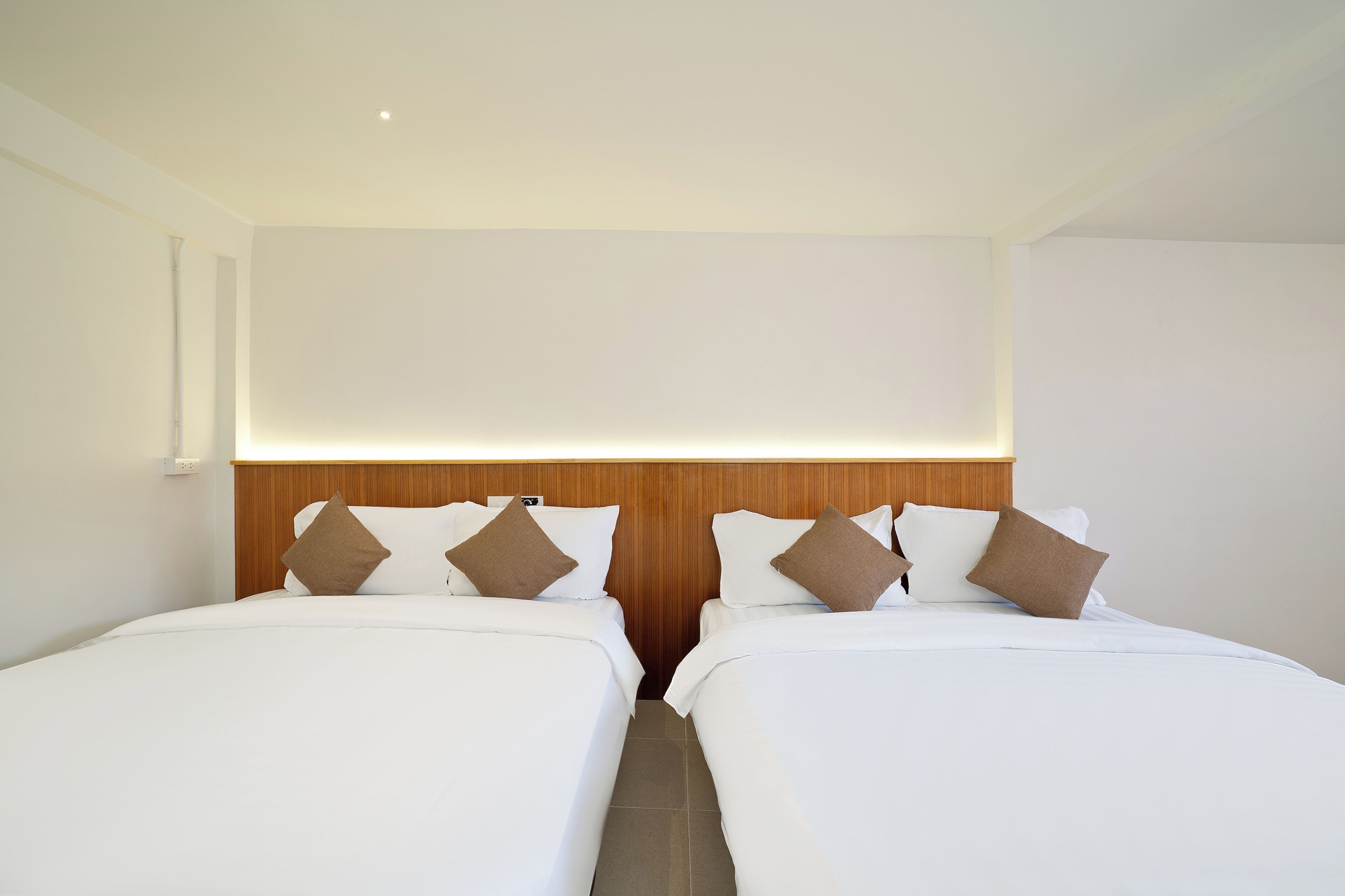 Une chambre d’hôtel avec deux lits, une tête de lit en bois et une petite lampe fixée au mur.