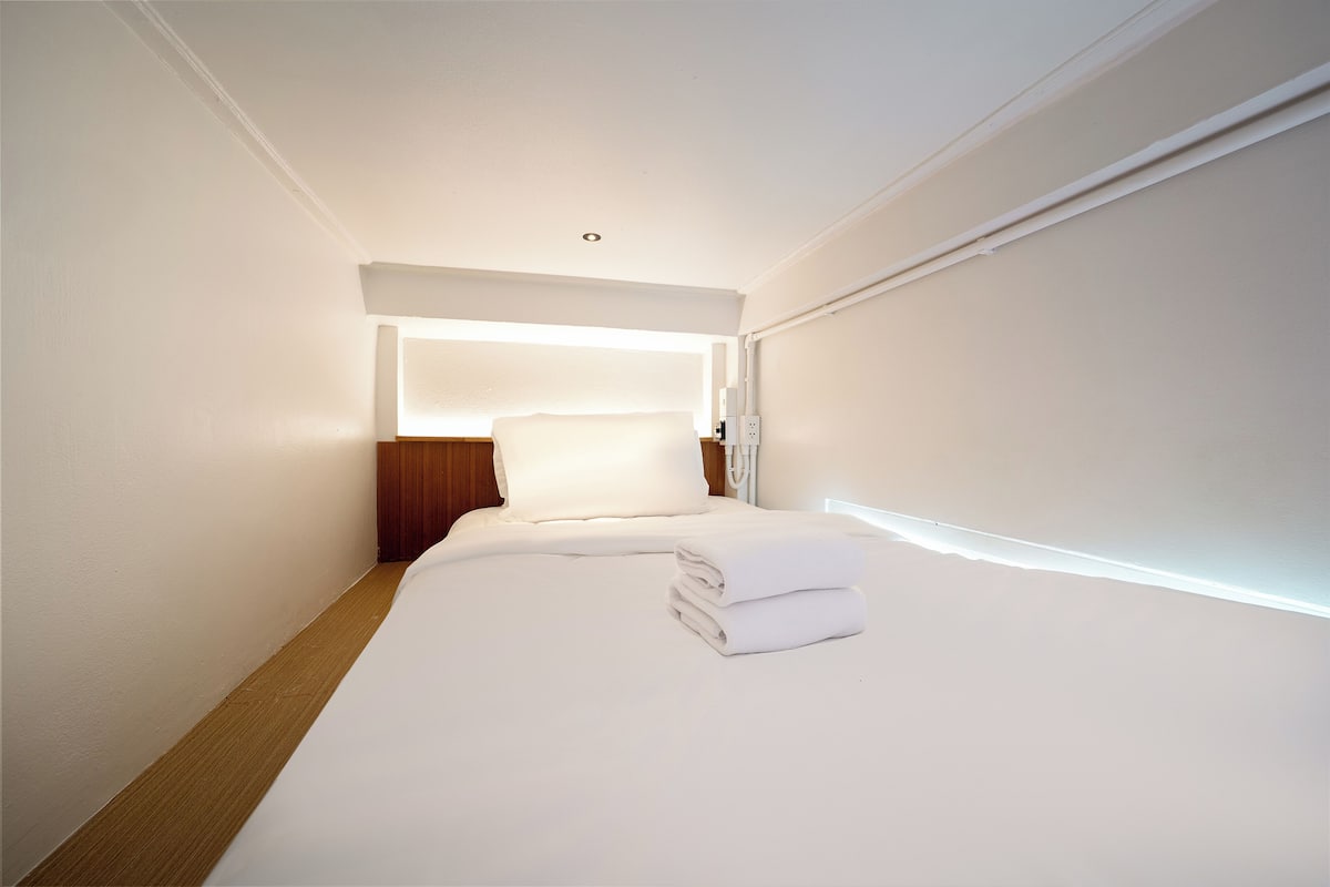 A hotel room with a neatly made bed, a wooden headboard, and a bright ceiling light.