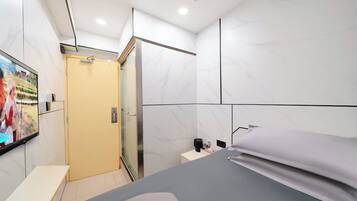 A modern hotel room with a bed, a desk, and a TV on the wall.