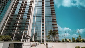Een modern hoog gebouw met een glazen gevel, een verharde looppad en buitenzitplaatsen.