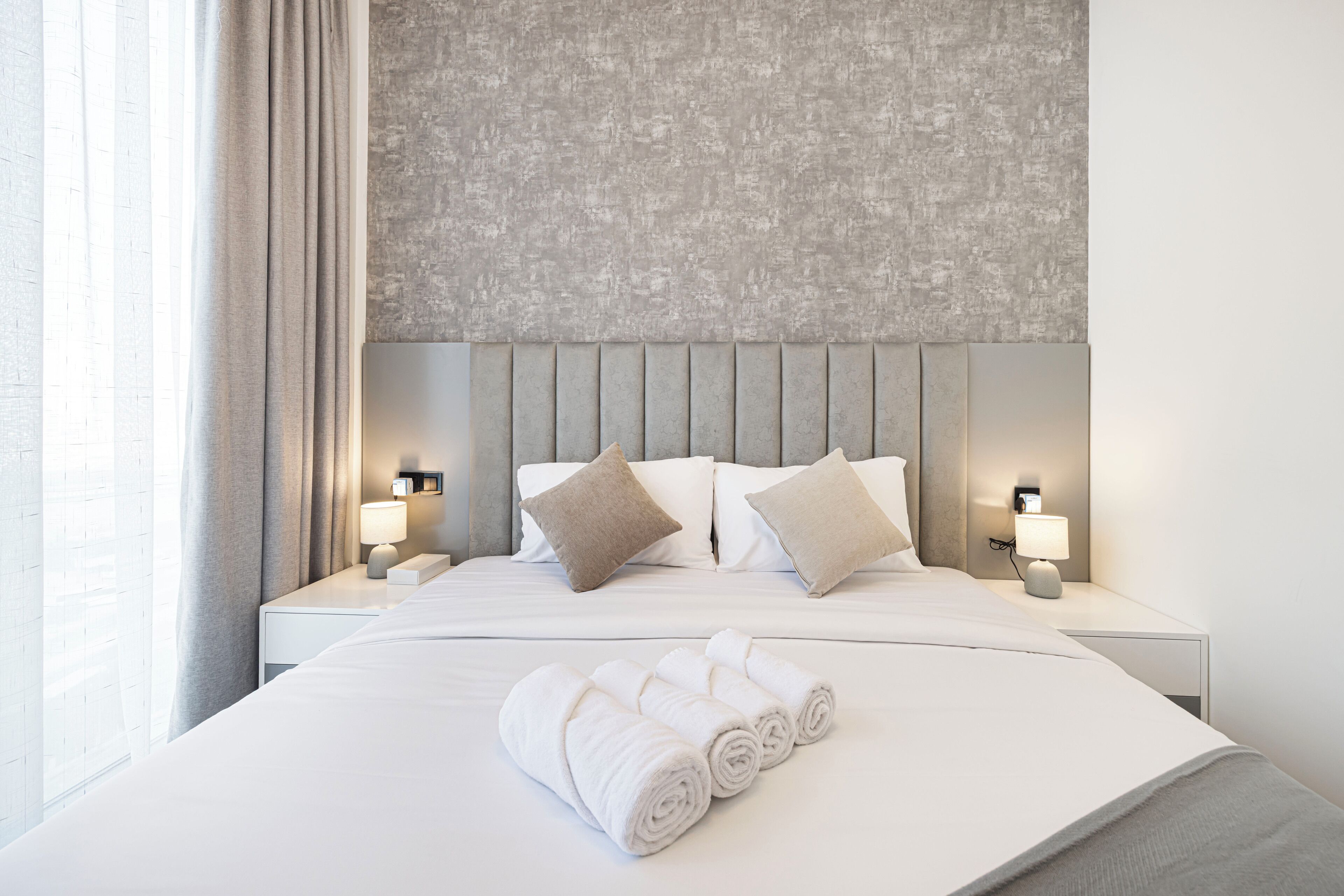A hotel room with a large bed, two bedside tables with lamps, a headboard, and a window with curtains.