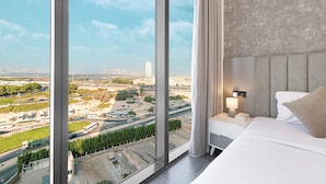 Een moderne hotelkamer met een groot raam met uitzicht op de stad, een opgemaakt bed en een nachtkastje met een lamp.
