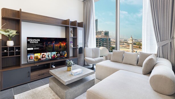 Een moderne woonkamer met een grote flatscreen televisie, een bank, een salontafel en een uitzicht op de skyline door grote ramen.