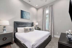 A bedroom with a large bed, two bedside tables, a nightstand, a wall-mounted TV, and a window with patterned curtains. - Gulf Views, Pvt Pool, Golf Cart, Steps To Beach! (Santa Rosa Beach)