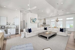 A spacious living area with a large sectional sofa, a coffee table, and a modern kitchen in the background. - Gulf Views, Pvt Pool, Golf Cart, Steps To Beach! (Santa Rosa Beach)