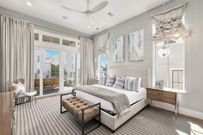 Un dormitorio con cama, escritorio, silla, ventana con cortinas y una obra de arte en la pared.