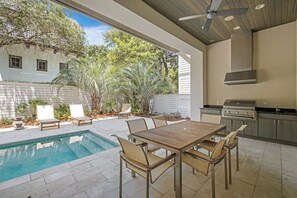 Un patio exterior con piscina, mesa de comedor, sillas y zona de barbacoa.