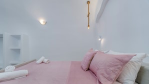 Quarto moderno com cama, almofadas, toalha e luminária na parede.